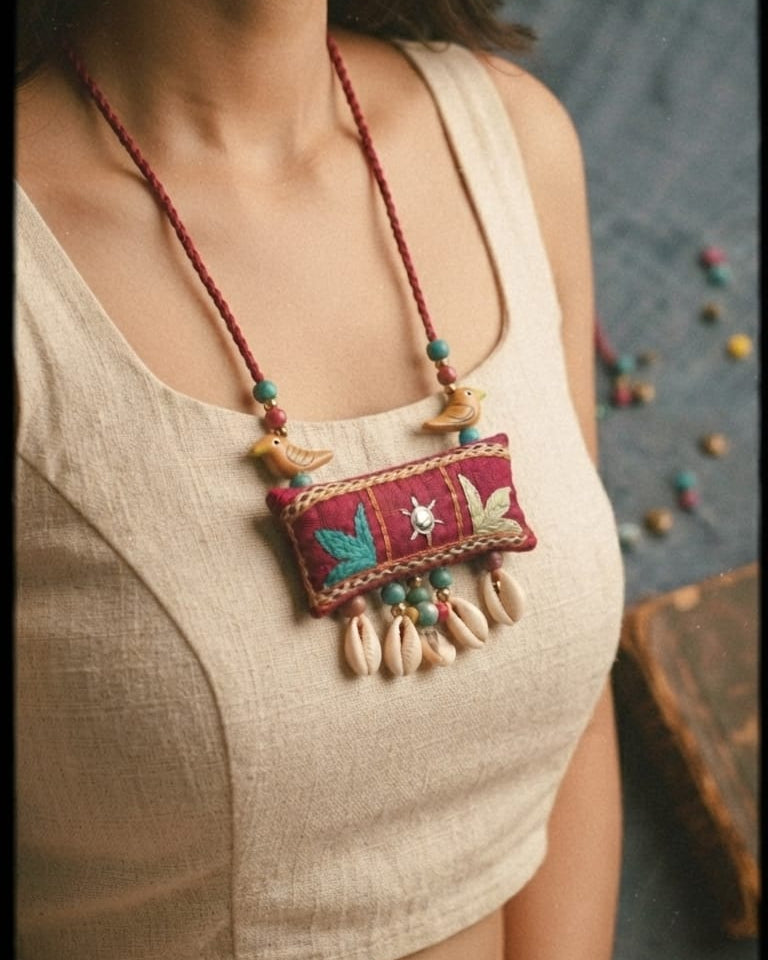 bohemian-style embroidered necklace with a red patch, colorful bead details, and dangling cowrie shells 