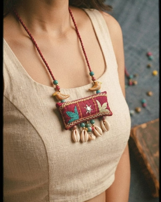 bohemian-style embroidered necklace with a red patch, colorful bead details, and dangling cowrie shells 